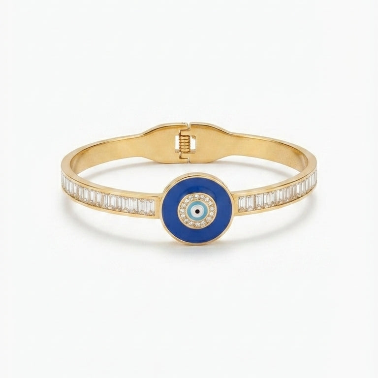 A gold bangle bracelet featuring a central blue circular evil eye charm and a row of small clear stones along the band, set against a plain white background.
