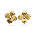 A pair of textured gold flower-shaped earrings with small clear center stones, displayed on a white marble pedestal with a gold rim against a softly blurred beige background.