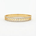 A gold bangle bracelet featuring a textured chevron pattern with pavé-set clear stones on the front, shown against a plain white background.