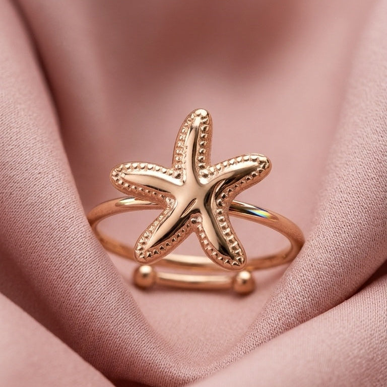 A rose gold starfish ring resting on draped dusty pink satin fabric.