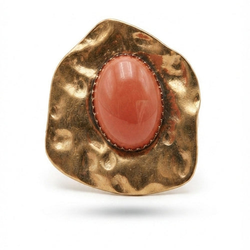 A textured gold ring featuring a large, polished oval coral cabochon stone in the center, set against a plain white background.