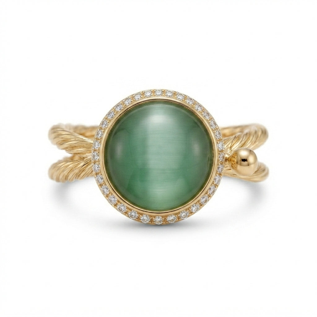 A gold ring featuring a large oval green cabochon gemstone surrounded by a halo of small clear stones, with a twisted gold band.