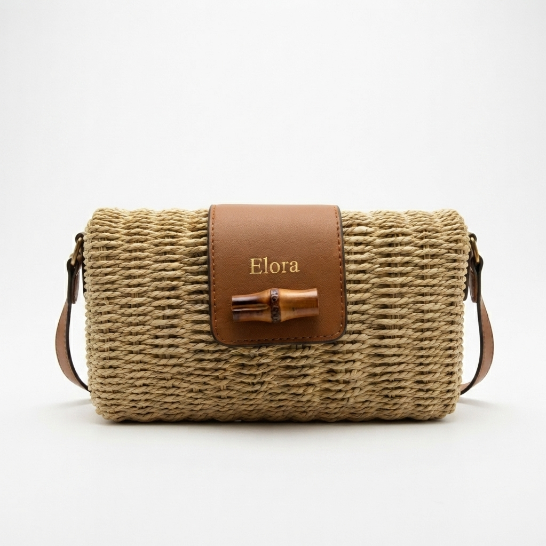 A woven straw shoulder bag with a brown leather front flap featuring the name 'Elora' in gold and a bamboo-style clasp, set against a plain white background.